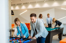 A group of coworkers playing foosball and billiards in office break room