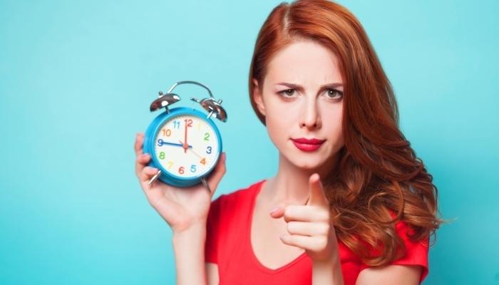 Redhead girl with alarm clock on blue background