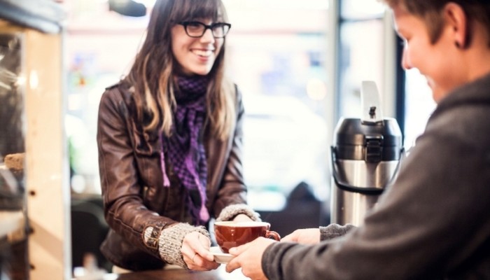 Smiling coffee shop worker hands latte to customer
