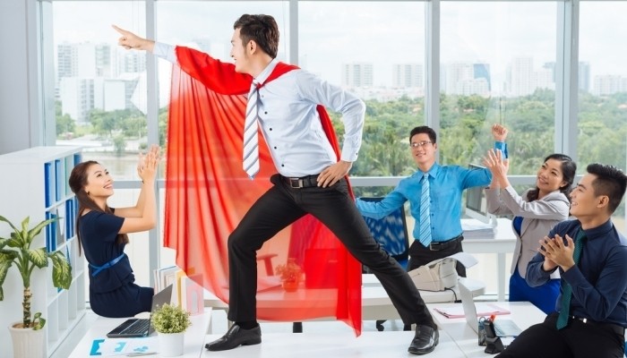 Manager in a red cape posing in front of his colleagues