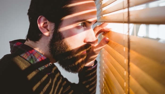 Young man looking through blinds