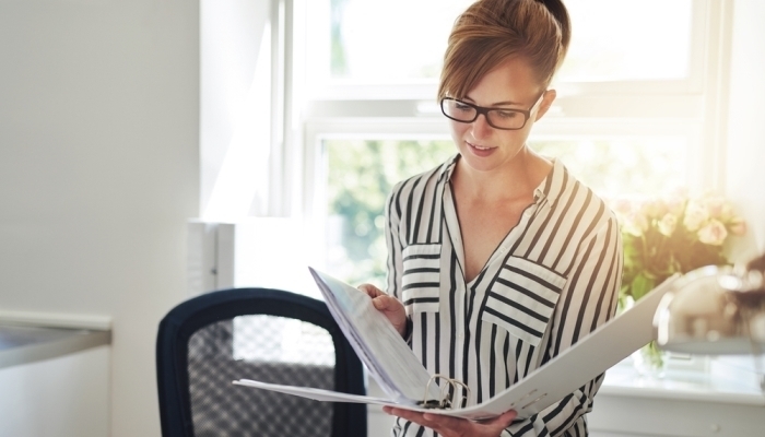 woman standing in her home office reading notes in an office binder