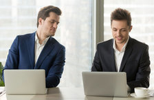 Curious, jealous businessman peering over coworker&#39;s laptop