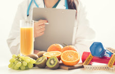 Female dietitian holding a clipboard with fruit and dumbbells placed on a desk