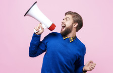 Cheerful young man shouting into a megaphone against a pink background