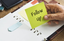 Close-up of a man's holding a sticky note that has the phrase 'follow up' written on it