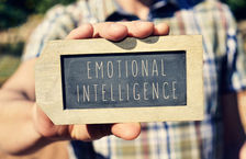 Close-up of a man holding a lapel-shaped chalkboard that has 'emotional intelligence' written on it