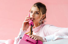 A young woman speaking on a pink landline telephone