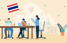 Illustration of two people working on their laptops and sitting at a desk and another woman standing there while holding a tablet, there is a backdrop of Bangkok and the Thai flag